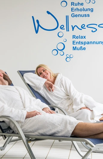 Das Bergische-2020-100-Gesundheit.jpg Entspannte Menschen in Bademänteln liegen auf Wellnessliegen im Spa-Bereich und lächeln einander an.