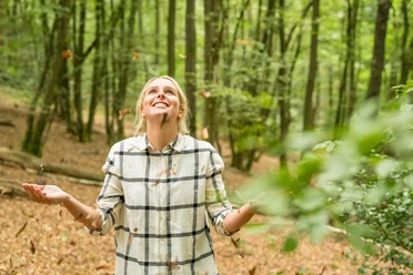 Waldbaden Frau in kariertem Hemd genießt lachend einen Herbstspaziergang im Wald unter fallendem Laub.