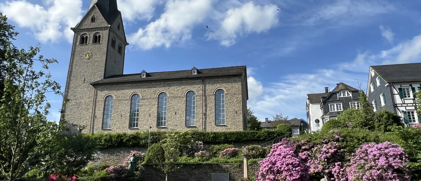 evangelische Kirche <p>Historische Kirche in Wiehl mit blühenden Rhododendren und blauem Himmel im Hintergrund.</p>