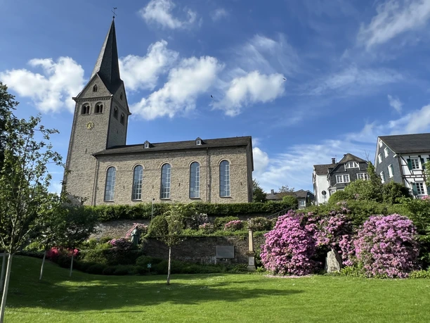 evangelische Kirche <p>Historische Kirche in Wiehl mit blühenden Rhododendren und blauem Himmel im Hintergrund.</p>