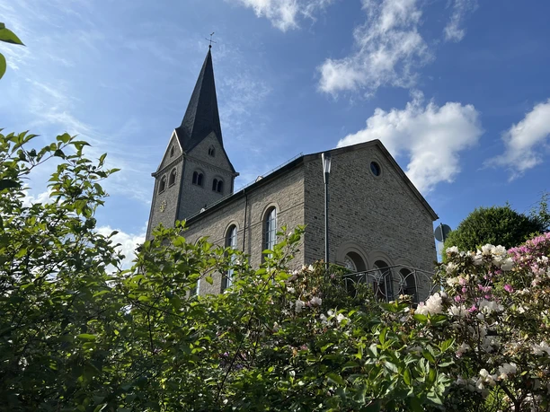 evangelische Kirche Kirche mit hohem Turm und blühenden Büschen im Vordergrund, blauer Himmel im Hintergrund.