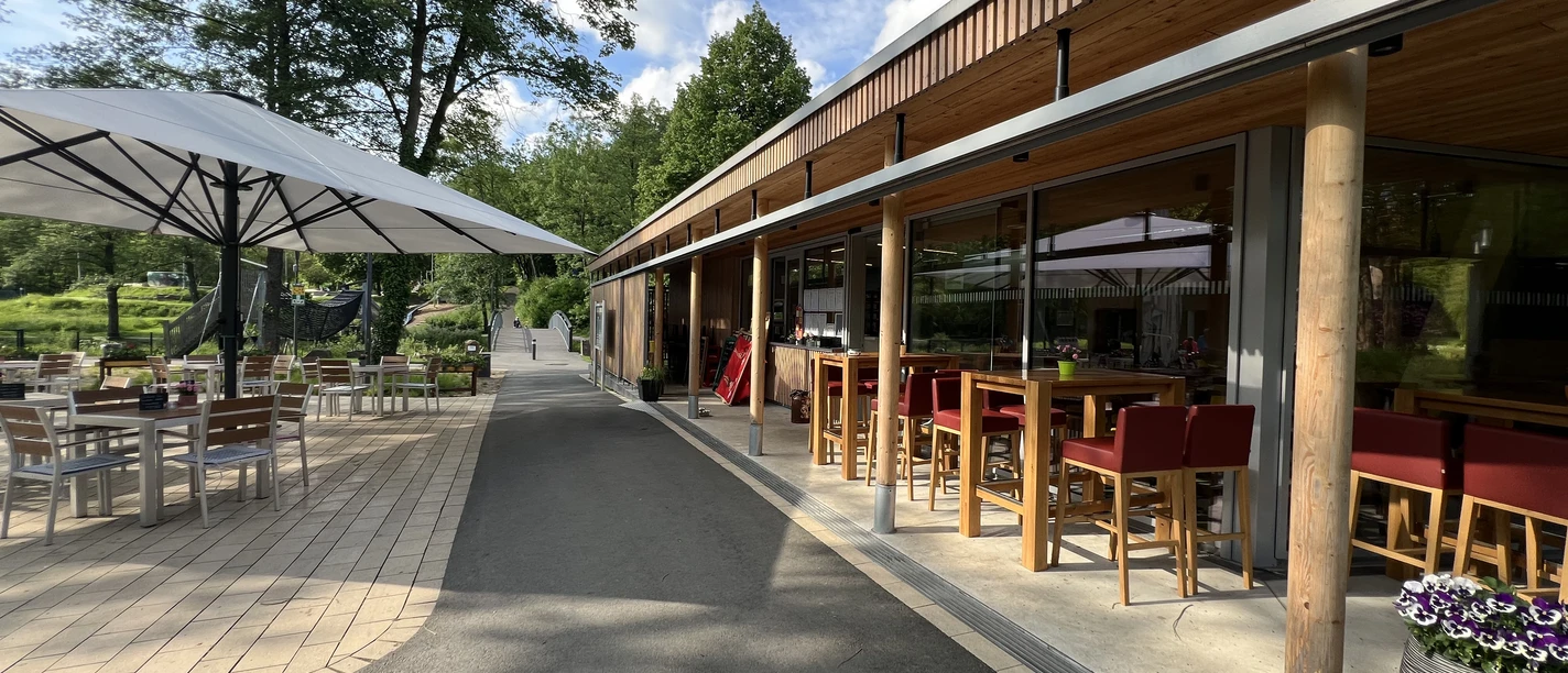Bistro im Wiehlpark <p>Ein Café mit Terrasse, roten Hochstühlen und Tischen im Freien, unter großen Sonnenschirmen.</p>