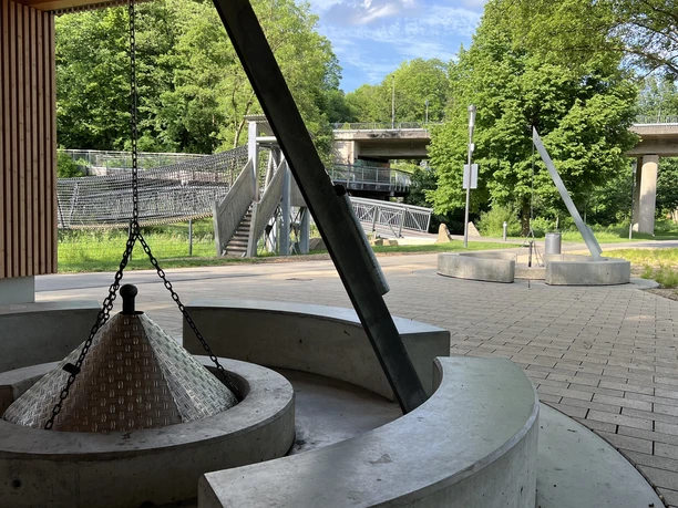 Grillplatz im Wiehlpark <p>Moderner Platz mit geometrischen Betonbänken, Skulpturen und grünem Hintergrund unter Brücken.</p>