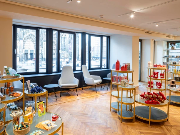 Tourist Information Köln Innenansicht der Kölner Tourist-Information mit Souvenirs und Domansicht durch Fenster.