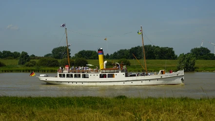 Prinz Heinrich auf der Ems.JPG Das weiße Dampfschiff Prinz Heinrich mit gelbem Schornstein fährt auf der Ems vor grünem Ufer.