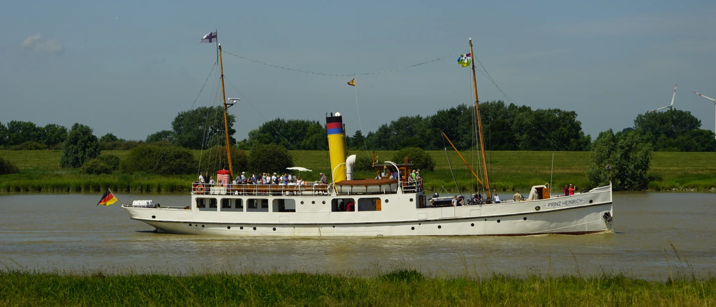 Prinz Heinrich auf der Ems.JPG Das weiße Dampfschiff Prinz Heinrich mit gelbem Schornstein fährt auf der Ems vor grünem Ufer.