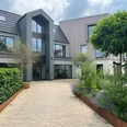 Ein modernes Gebäude mit großen Fenstern, umgeben von gepflegtem Grün und einer gepflasterten Einfahrt.