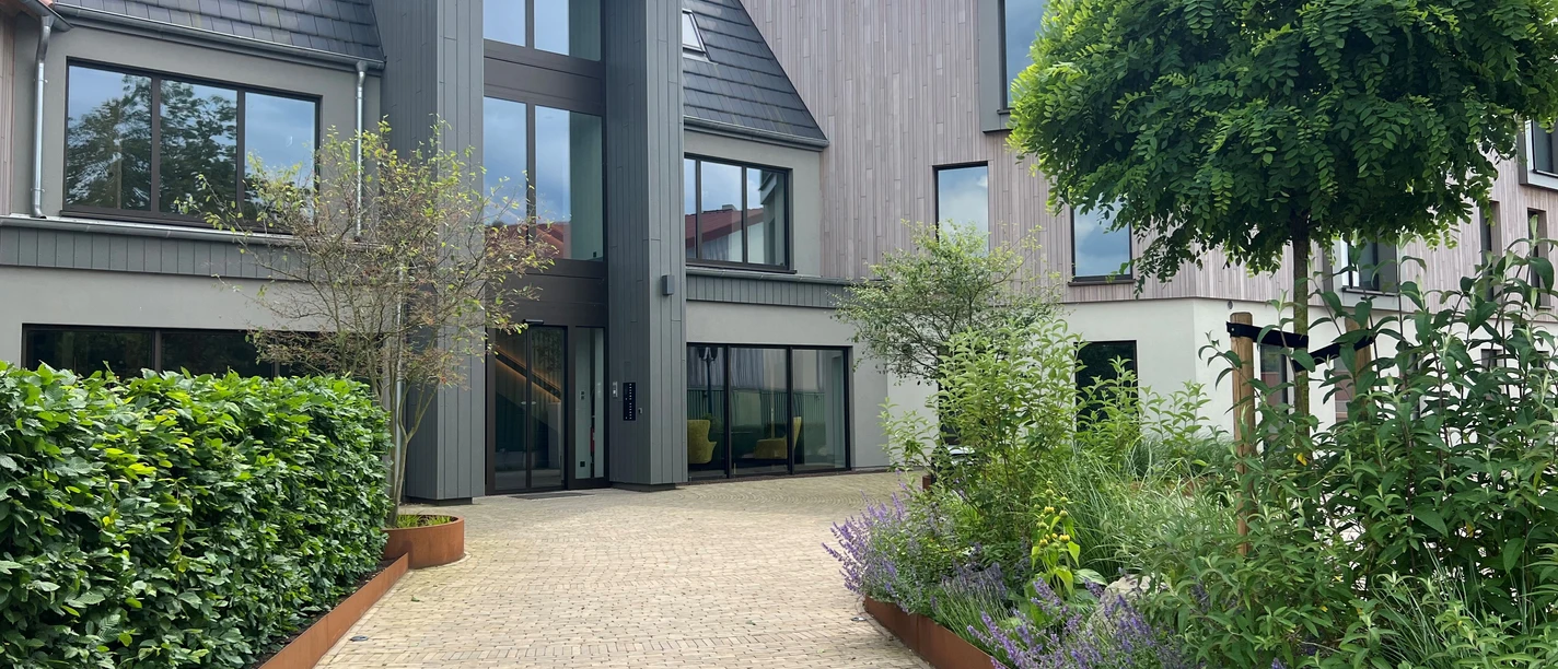 Thöles in Bücken Ein modernes Gebäude mit großen Fenstern, umgeben von gepflegtem Grün und einer gepflasterten Einfahrt.