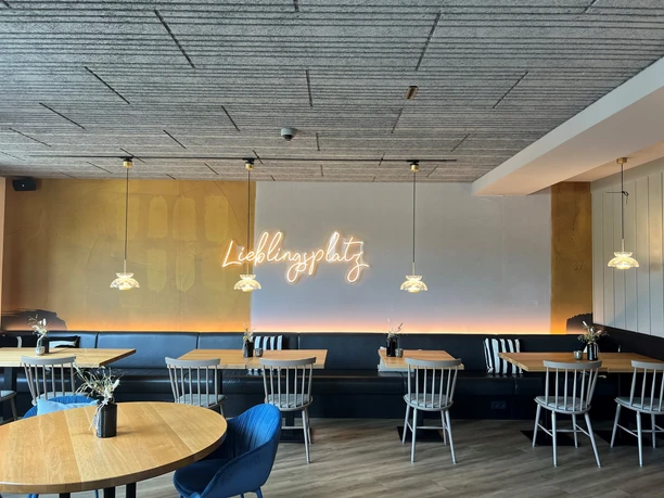A modern café with wooden tables, black benches and decorative ceiling lights.