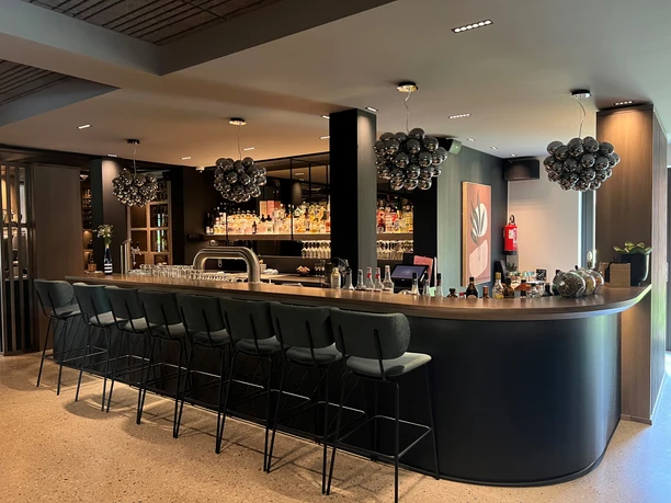 A modern bar with a high counter, black bar stools and decorative light globes on the ceiling.