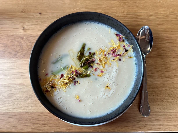 Spargelsuppe.jpg Eine cremige Spargelsuppe in einer dunklen Schüssel, dekoriert mit essbaren Blüten und Spargelstücken.