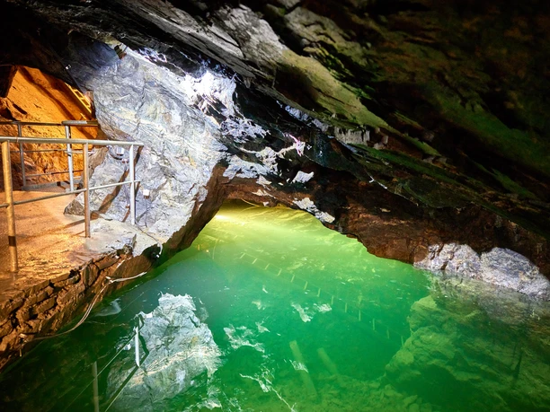Podzemní jezero v osvětleném a přístupném tunelu s třpytivou tyrkysově zbarvenou vodou.