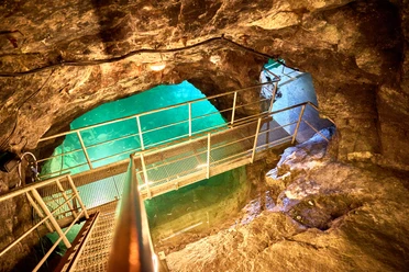 Unterirdischer See im Marie Louise Stolln.jpg Metallbrücke überspannt türkisfarbenen See in natürlichen, von Felsen umgebenen, unterirdischem Raum.