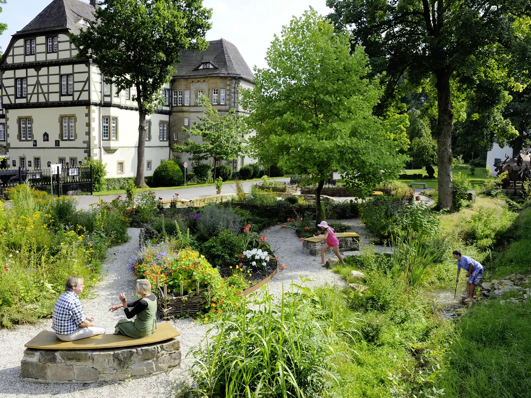 Menschen genießen den gepflegten Schulklostergarten Neuenheerse, umgeben von historischen Gebäuden.