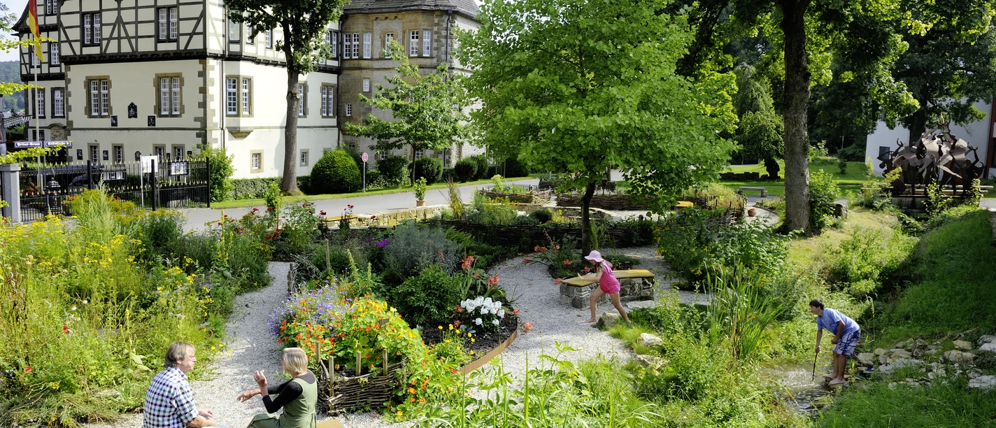 Menschen genießen den gepflegten Schulklostergarten Neuenheerse, umgeben von historischen Gebäuden.