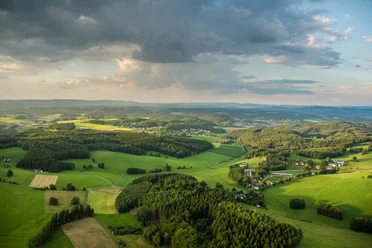 Reichshof Blockhaus Luftaufnahme einer grünen Hügellandschaft bei Reichshof unter bewölktem Himmel.