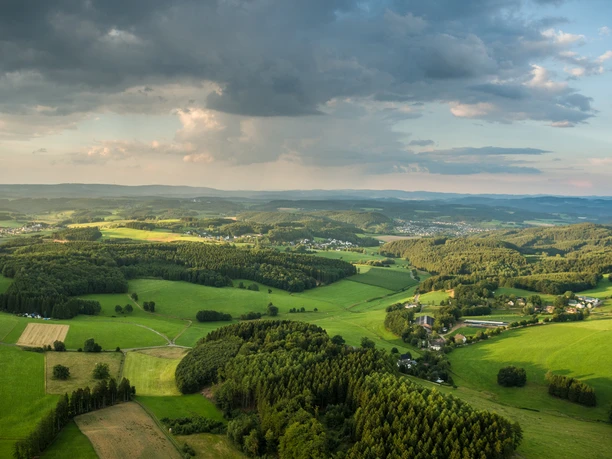 Reichshof Blockhaus Luftaufnahme einer grünen Hügellandschaft bei Reichshof unter bewölktem Himmel.