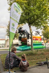 Green World Tour Cologne A father and child sit on a meadow in front of a green cow-shaped bouncy castle at the Green World Tour.