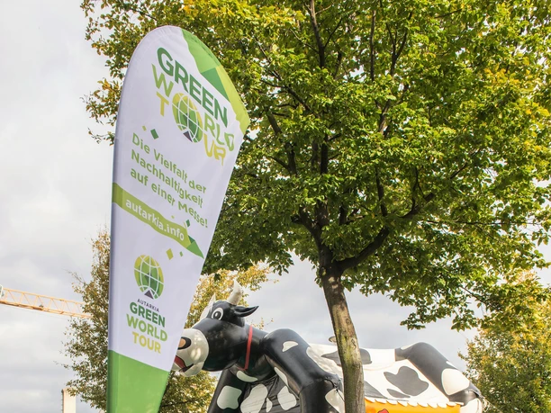 Green World Tour Cologne A father and child sit on a meadow in front of a green cow-shaped bouncy castle at the Green World Tour.