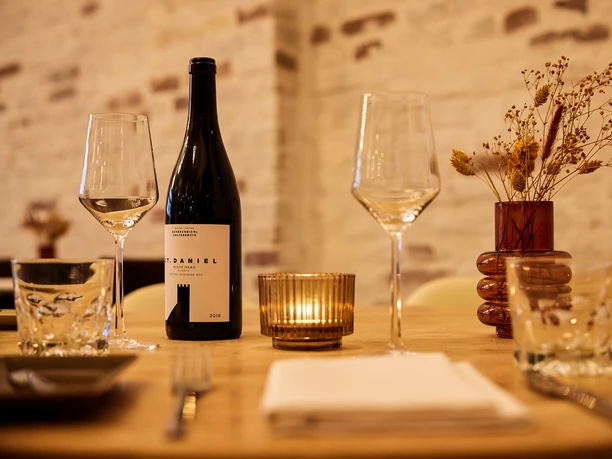 Gasthaus Stromberg, Waltrop <p>Elegant gedeckter Tisch mit Weinflasche, Gläsern und Kerzenlicht vor einer rustikalen Backsteinwand.</p>