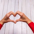 Female hands making a heart shape on a white wooden background. Female hands making a heart shape on a white wooden background.