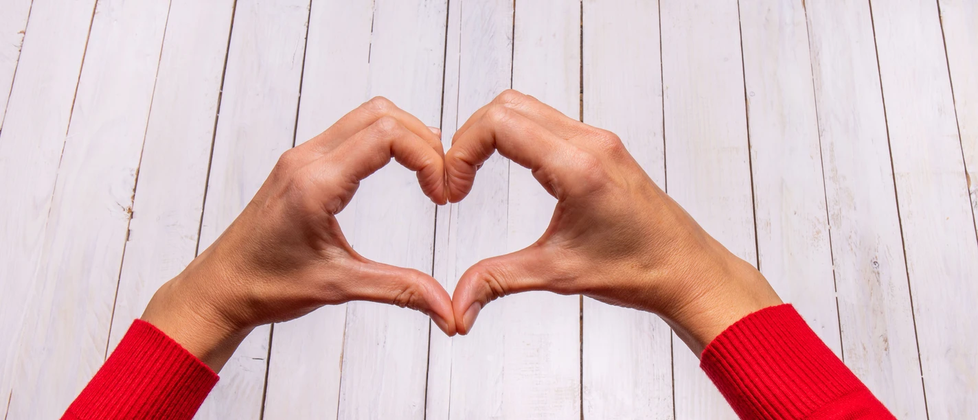 Female hands making a heart shape on a white wooden background. Female hands making a heart shape on a white wooden background.
