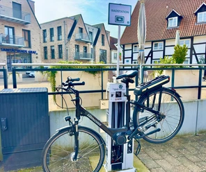 Fahrradstation mit aufgeladenem E-Bike in urbaner Umgebung, umgeben von modernen und traditionellen Gebäuden.