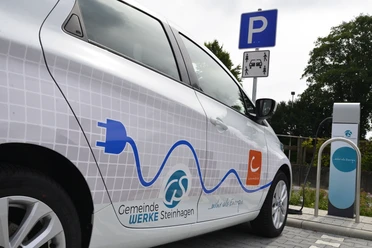 Mobilstation Steinhagen eAuto Ein Elektroauto der Gemeindewerke Steinhagen wird an einer Ladestation auf einem Parkplatz geladen.