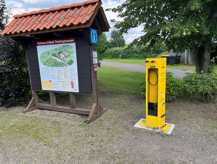 ADAC-Radservicestation ADAC-Radservicestation neben Infotafel mit Schlosskarte; umgeben von Bäumen und Schotterweg.
