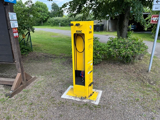 An ADAC bike service station in bright yellow, equipped with a bike pump and tools, surrounded by trees.