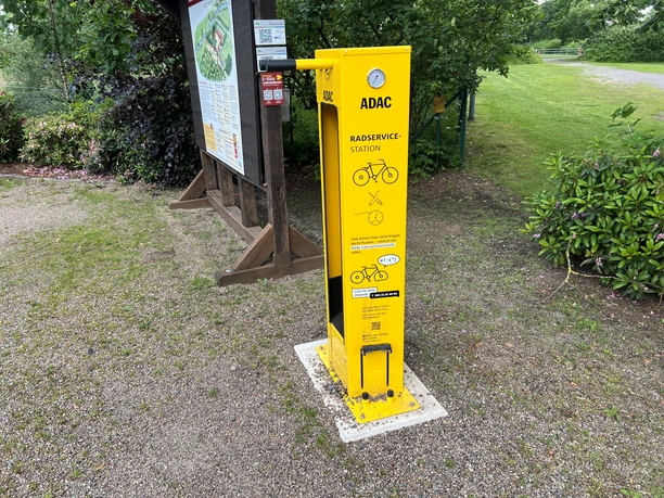 Leuchtend gelbe ADAC-Radservicestation mit Werkzeugen und Luftpumpe, umgeben von grüner Natur.