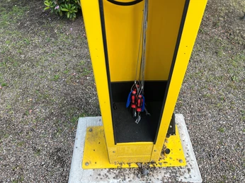 ADAC-Radservicestation Gelbe Radservicestation mit verschiedenen Werkzeugen, am Boden befestigt und von Kies umgeben.