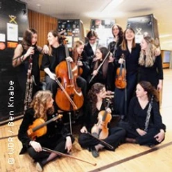 Gruppe junger Musikerinnen mit Streichinstrumenten in einem Saal während einer Probe