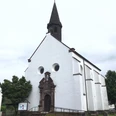 Katholische Kirche Blankenau mit markantem Turm, umgeben von Bäumen und gepflastertem Weg.