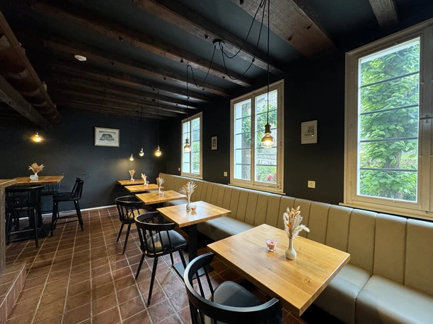 Zum Haus Olpe - Ansicht Innenbereich Gemütlicher Café-Raum mit Holztischen, modernen Stühlen und gedämpfter Beleuchtung, ideal zum Entspannen.