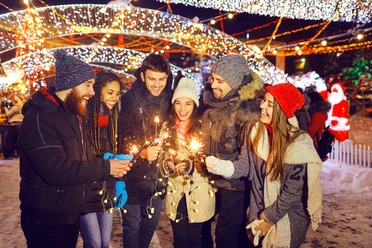 Happy friends with sparklers at a fair at christmas Teamfoto auf dem Weihnachtsmarkt: Personen halten Wunderkerzen in den Händen