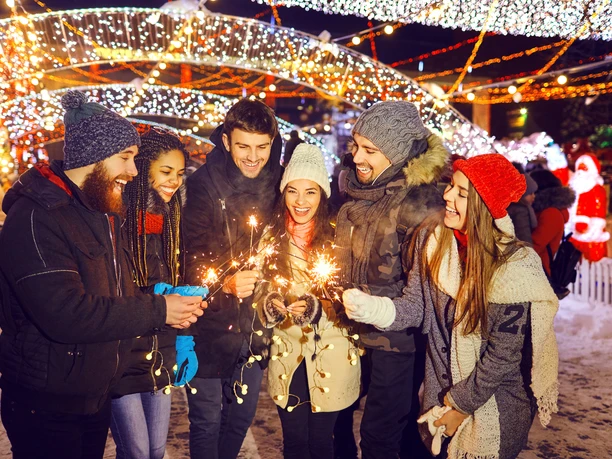 Happy friends with sparklers at a fair at christmas Teamfoto auf dem Weihnachtsmarkt: Personen halten Wunderkerzen in den Händen