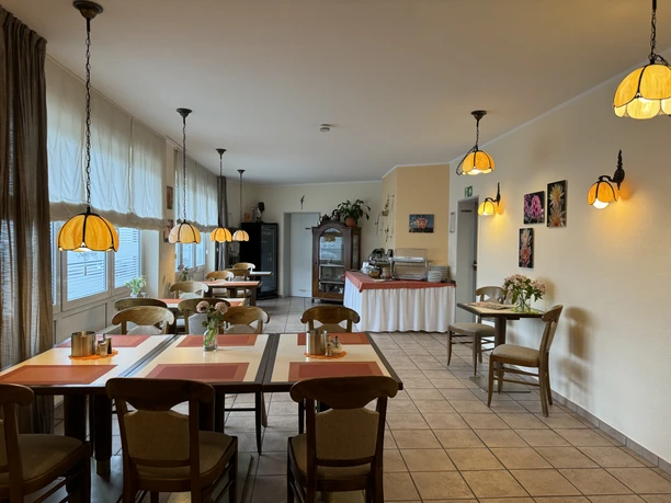 Hotel Garni Alt Refrath - Innenansicht Essbereich Gemütlicher Frühstücksraum mit Holzmöbeln, großen Fenstern und dekorativen Lampen, einladend und hell.