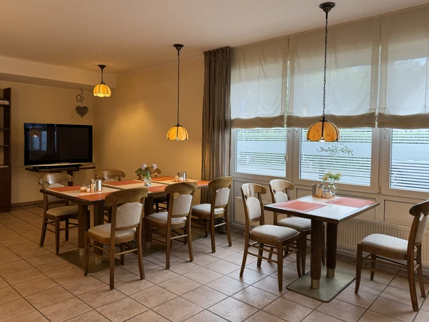 Hotel Garni Alt Refrath - Innenansicht Essbereich Gemütlicher Speiseraum mit hölzernen Tischen und Stühlen, dekorativen Lampen und großen Fenstern.