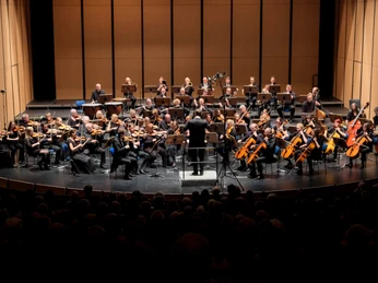 Sinfonieorchester Paderborn_Sinfoniekonzert-2024_Pressefoto 4.jpg Ein Sinfonieorchester spielt in einem Konzertsaal, dirigiert von einem schwarz gekleideten Dirigenten.