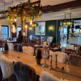 Kruegers_Gastraum_innen_01.jpg Ein rustikal eingerichteter Gastraum mit Holztischen, gemütlichen Stühlen und dekorativen Pelzkissen.A rustic dining room with wooden tables, cozy chairs and decorative fur cushions.En rustikt indrettet spisestue med træborde, hyggelige stole og dekorative pelspuder.Een rustiek ingerichte eetkamer met houten tafels, gezellige stoelen en decoratieve bontkussens.
