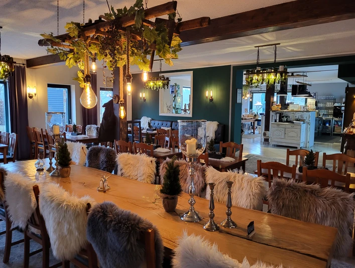 Kruegers_Gastraum_innen_01.jpg Ein rustikal eingerichteter Gastraum mit Holztischen, gemütlichen Stühlen und dekorativen Pelzkissen.A rustic dining room with wooden tables, cozy chairs and decorative fur cushions.En rustikt indrettet spisestue med træborde, hyggelige stole og dekorative pelspuder.Een rustiek ingerichte eetkamer met houten tafels, gezellige stoelen en decoratieve bontkussens.