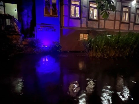Pfälzer Weinstube 2.jpg Traditionelle Fachwerkfassade bei Nacht, durch lila Licht beleuchtet, spiegelt sich im Wasser.
