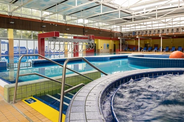 Friesentherme_69_klein.jpg Ein modernes Hallenbad mit mehreren Becken, Liegeflächen und einer gläsernen Decke.
