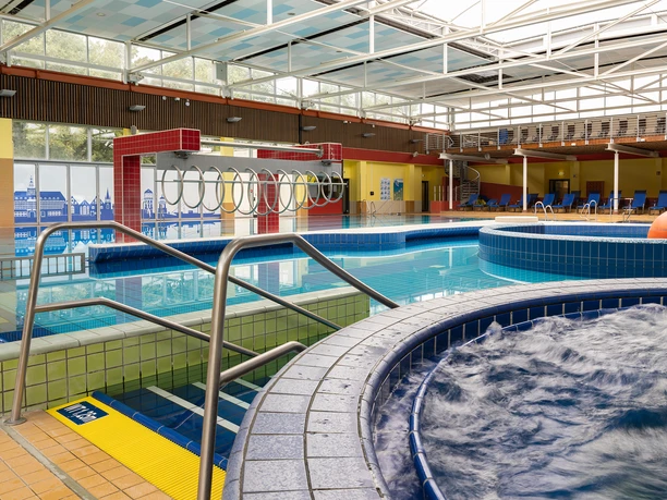 Friesentherme_69_klein.jpg Ein modernes Hallenbad mit mehreren Becken, Liegeflächen und einer gläsernen Decke.