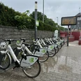 E-Bike Verleihstation am Bahnhof Rösrath Fahrradstation mit mehreren weißen Leihfahrrädern vor einem Bahnhof, umgeben von grünen Sträuchern.