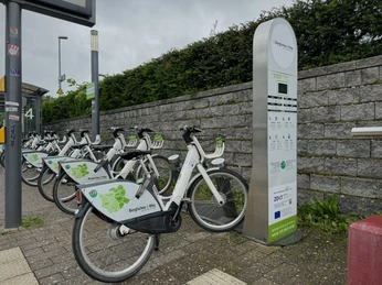 E-Bike Verleihstation Fahrradverleihstation mit weißen Leihrädern vor einer Steinmauer, bereit zur Nutzung.