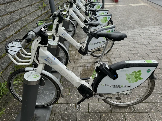 E-Bike Verleihstation Leihstation mit mehreren weißen Elektro-Fahrrädern der Marke "Bergisches e-Bike" an einer Straße.