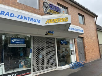 Zweiradzentrum Hertzig Fahrradgeschäft mit Ziegelsteinfassade, Schaufenster, Rolltor und Fahrradständer vor dem Eingang.