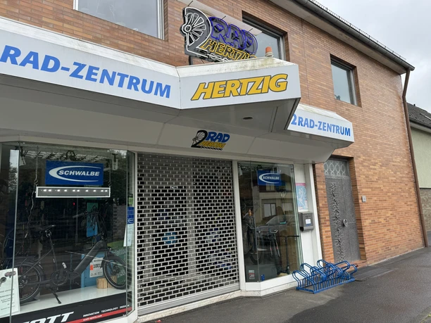 Zweiradzentrum Hertzig Fahrradgeschäft mit Ziegelsteinfassade, Schaufenster, Rolltor und Fahrradständer vor dem Eingang.